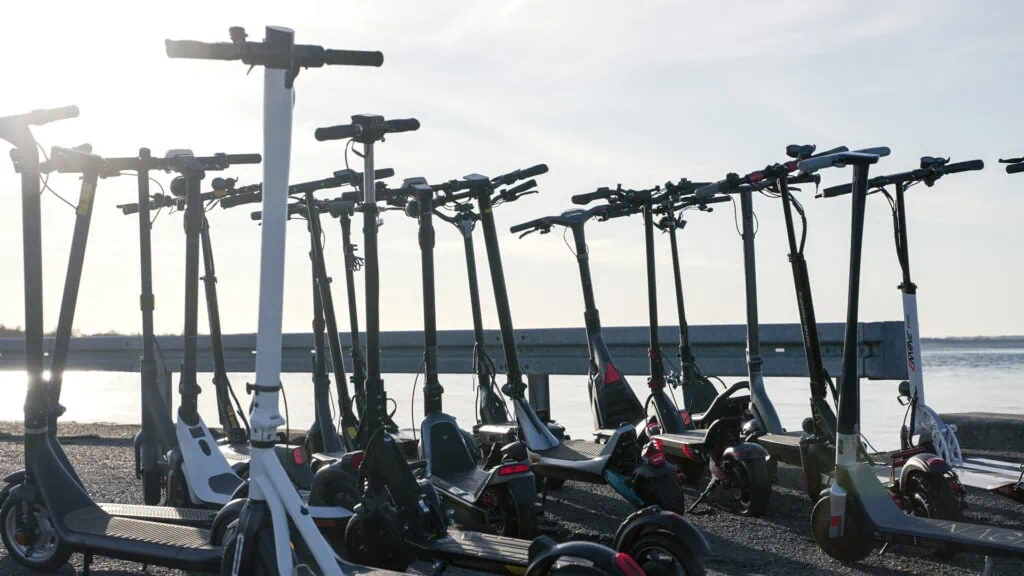 Buying Guide: How To Choose an Electric Scooter 17 Lineup of electric scooters on asphalt with the ocean in the background in golden hour